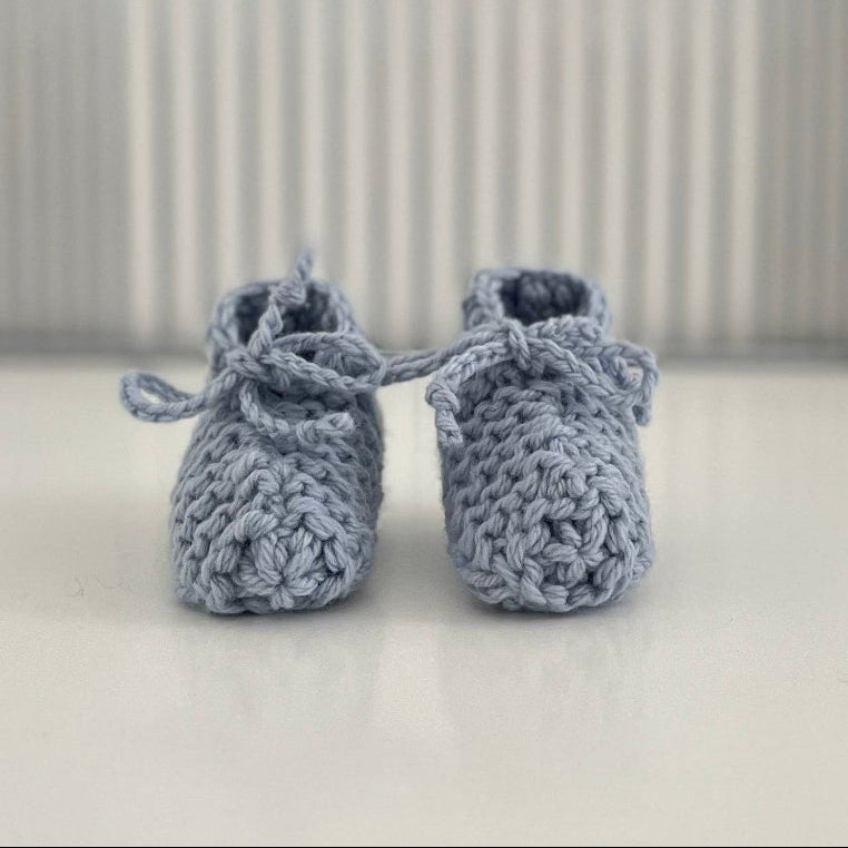 Pair of blue baby chunky knit booties on a white surface with a striped background