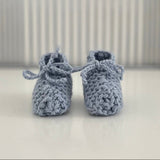 Pair of blue baby chunky knit booties on a white surface with a striped background