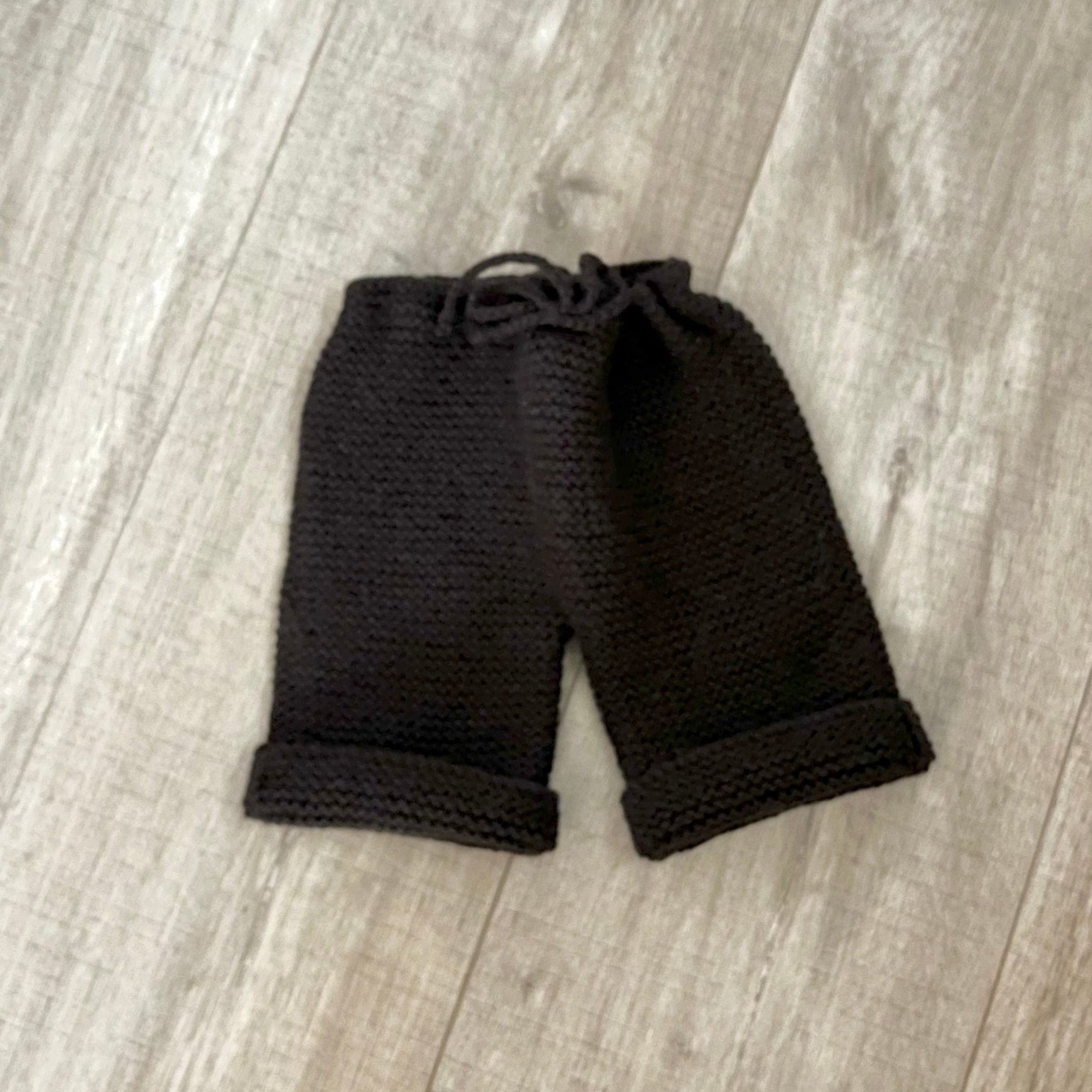 chocolate knit baby pants with a drawstring waist and rolled cuffs, laid flat on a light wood floor.