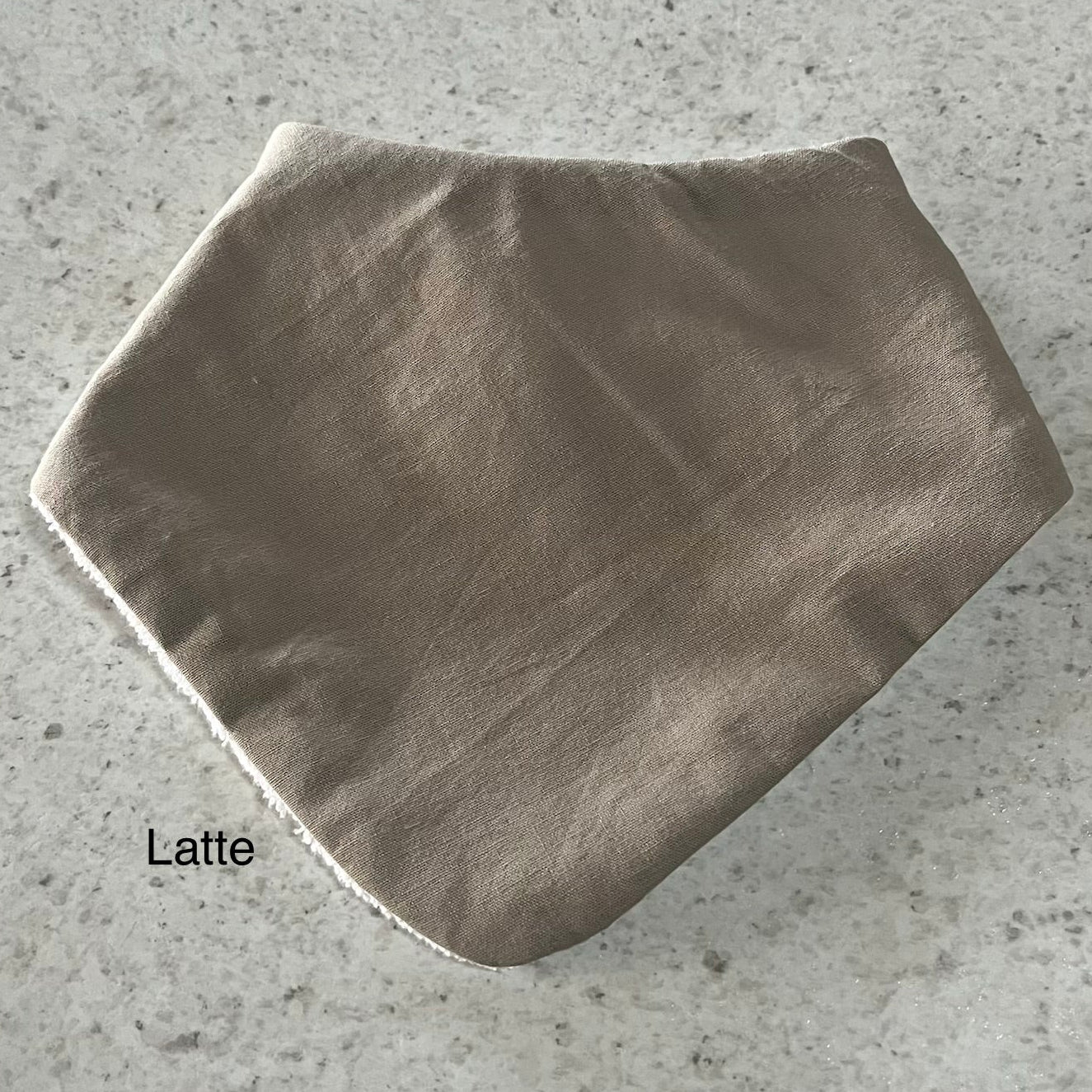 Latte coloured dribble bib on a grey concrete surface