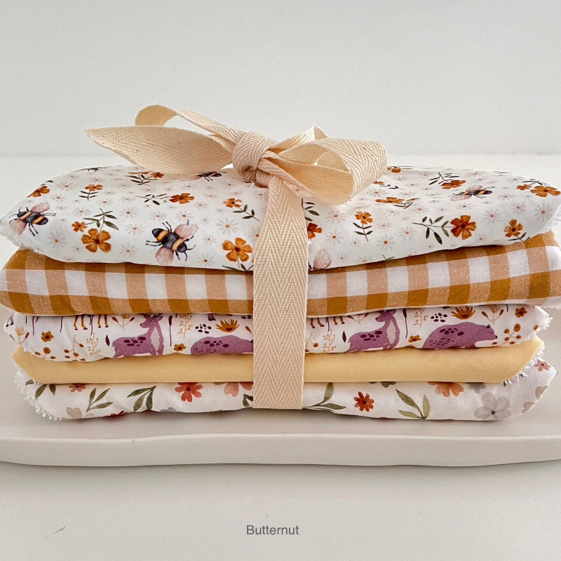 Stack of folded dribble bibs with floral and checkered patterns tied with a ribbon on a white surface.