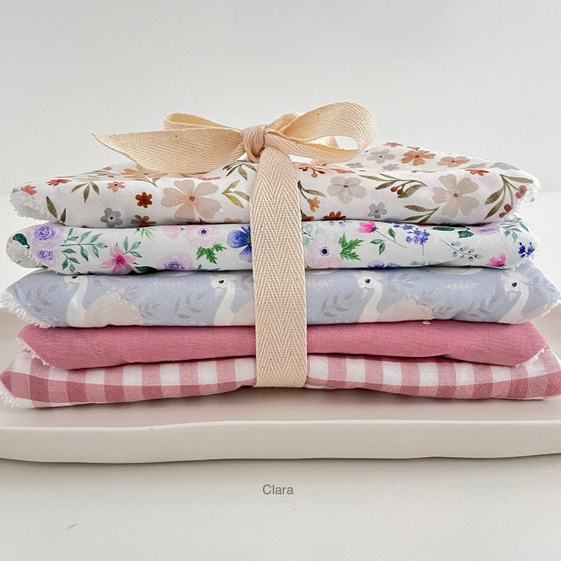 Stack of floral and checkered dribble bibs tied with a ribbon on a light background