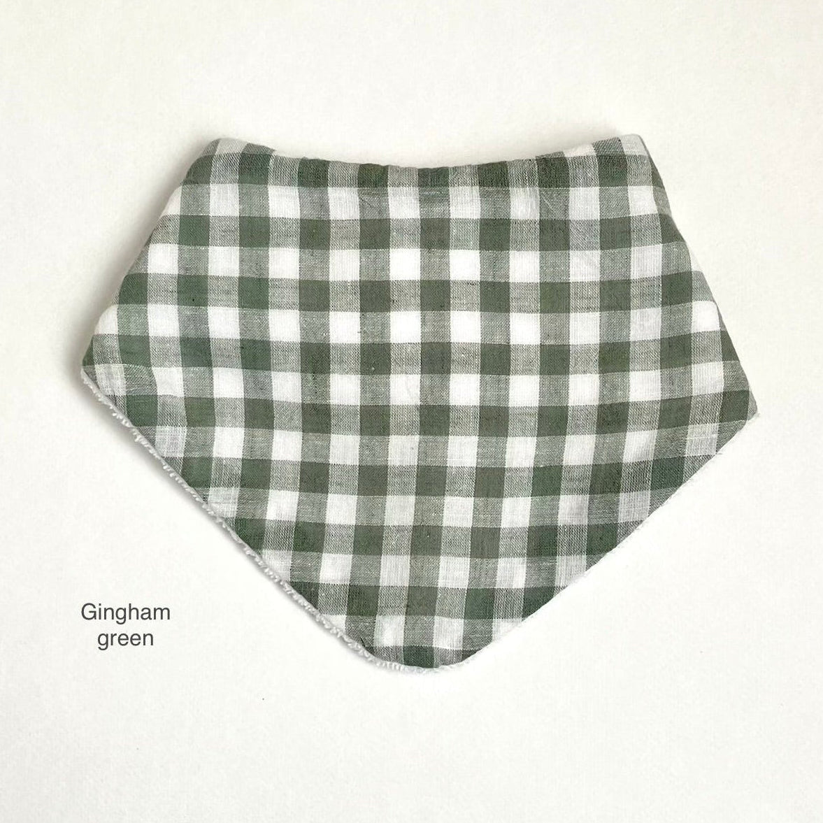 A triangular bandana bib in a gingham check pattern of gingham green and white, displayed flat against a light off-white background with 'Gingham green' text on the bottom left.