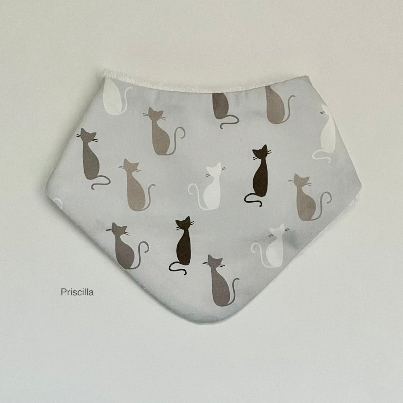 A light gray triangular bandana bib with an all-over pattern of black, white, and brown cat silhouettes, displayed flat against a light gray background.