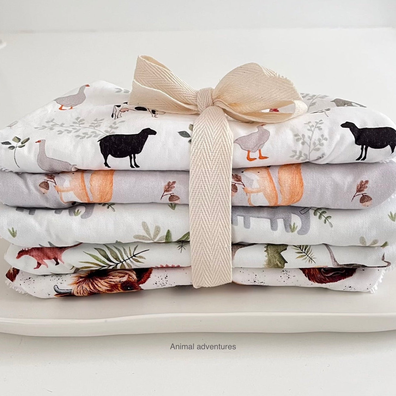 Stack of folded fabric with animal patterns tied with a ribbon on a white surface.