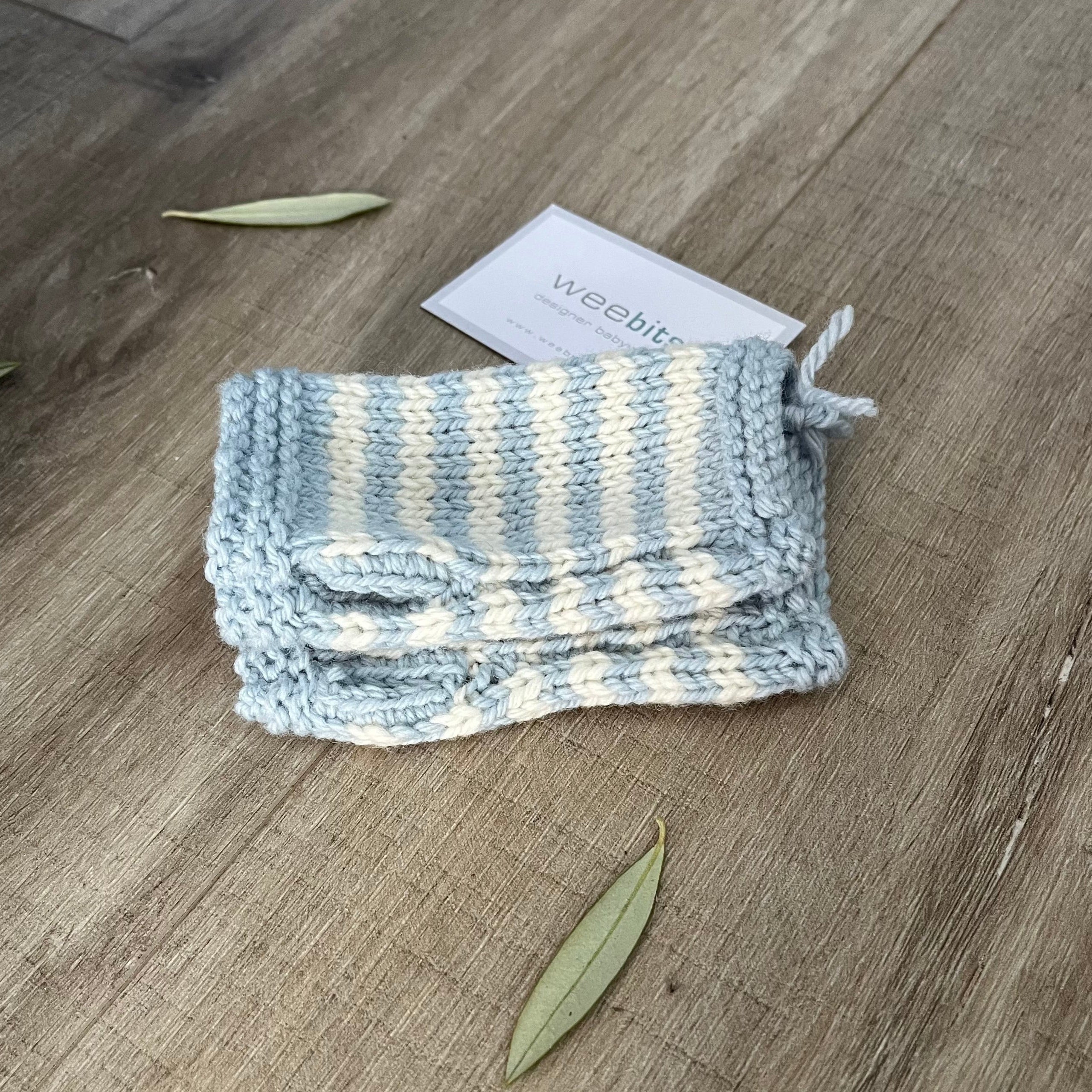 Knitted baby fingerless mittens with blue and white stripes on a wooden surface