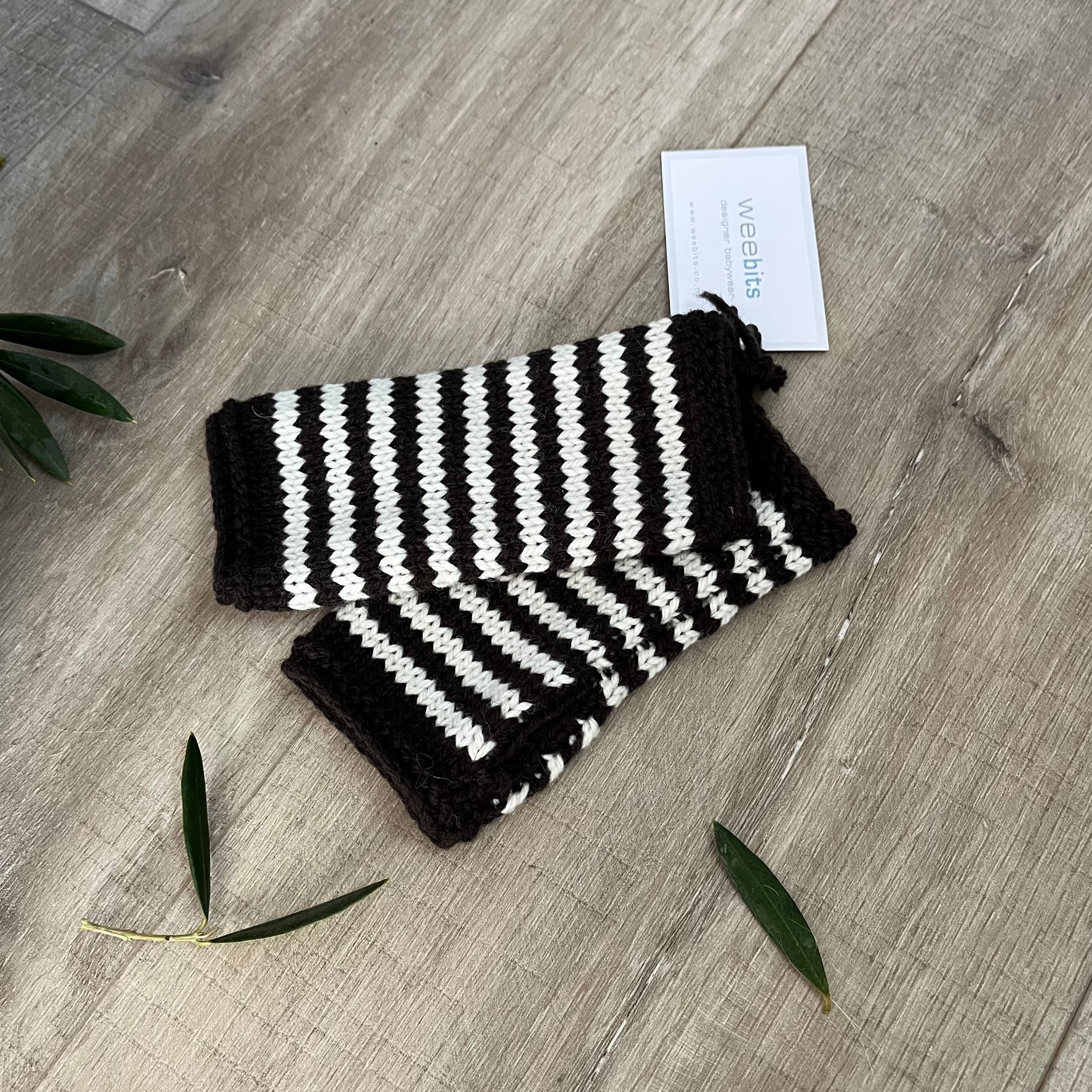 Knitted baby fingerless mittens with chocolate and white stripes on a wooden surface