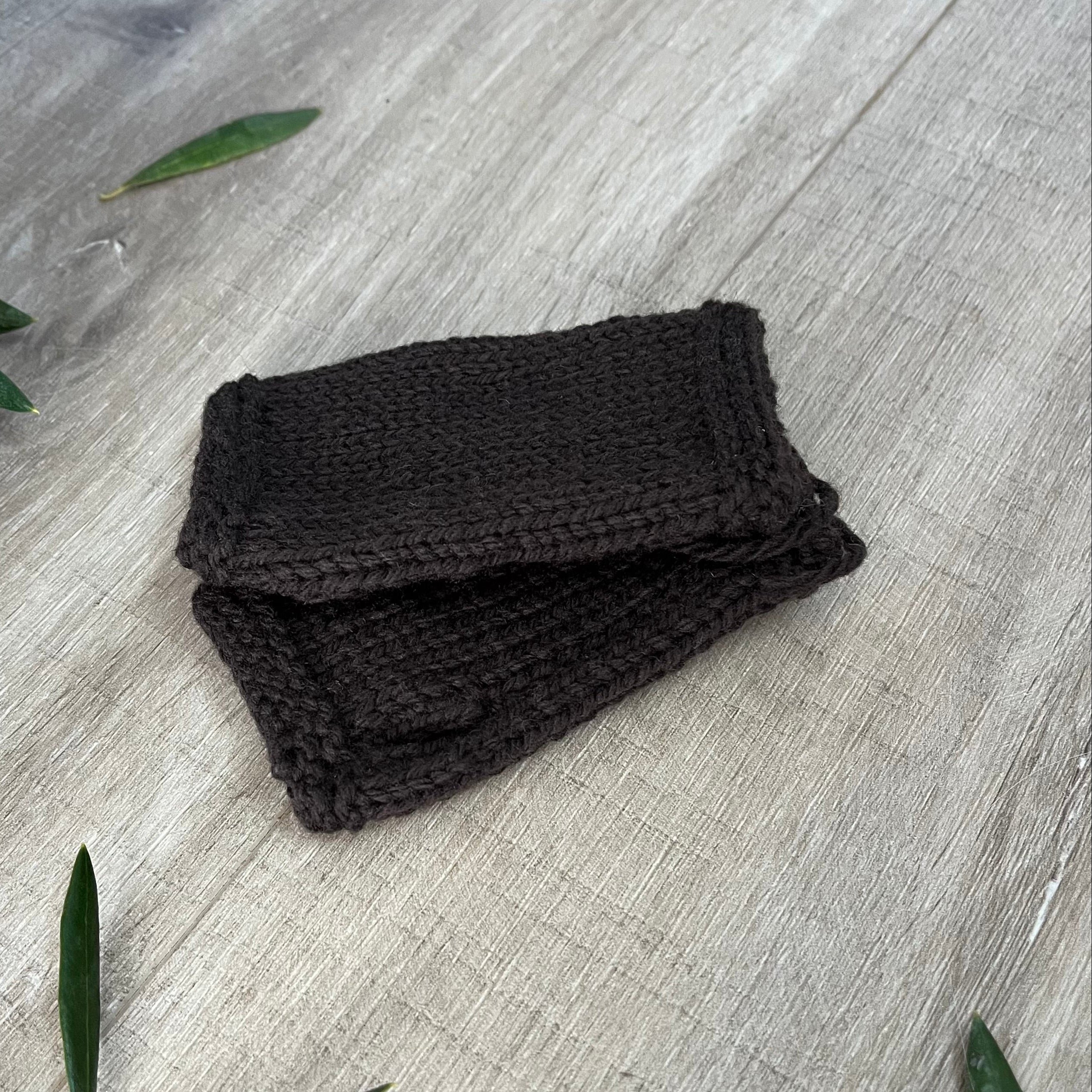 Chocolate knitted fingerless mittens on a wooden surface with olive leaves.
