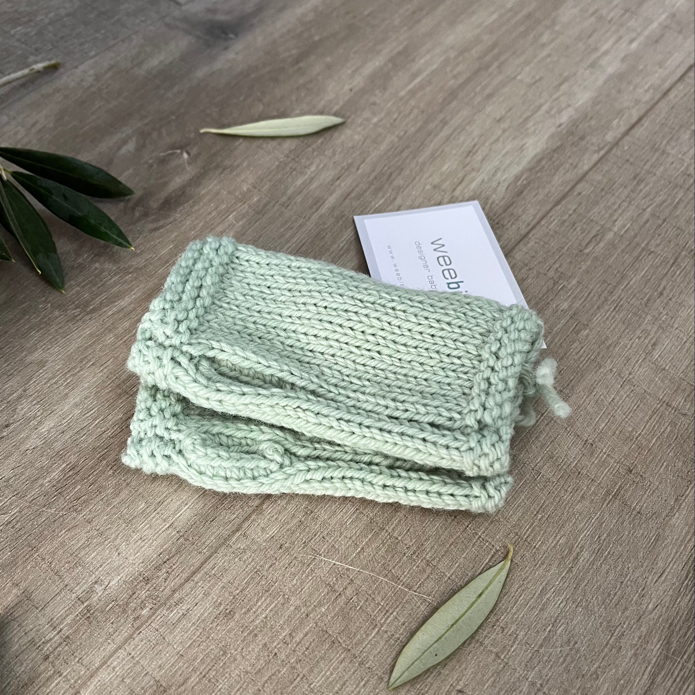 Mint knitted fingerless mittens on a wooden surface with olive leaves.
