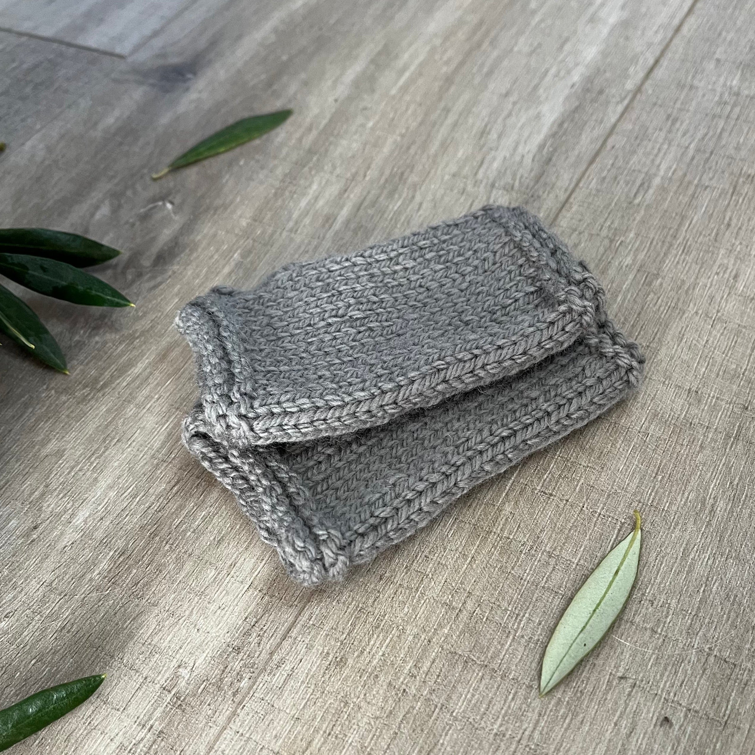 mushroom knitted fingerless mittens on a wooden surface with olive leaves.