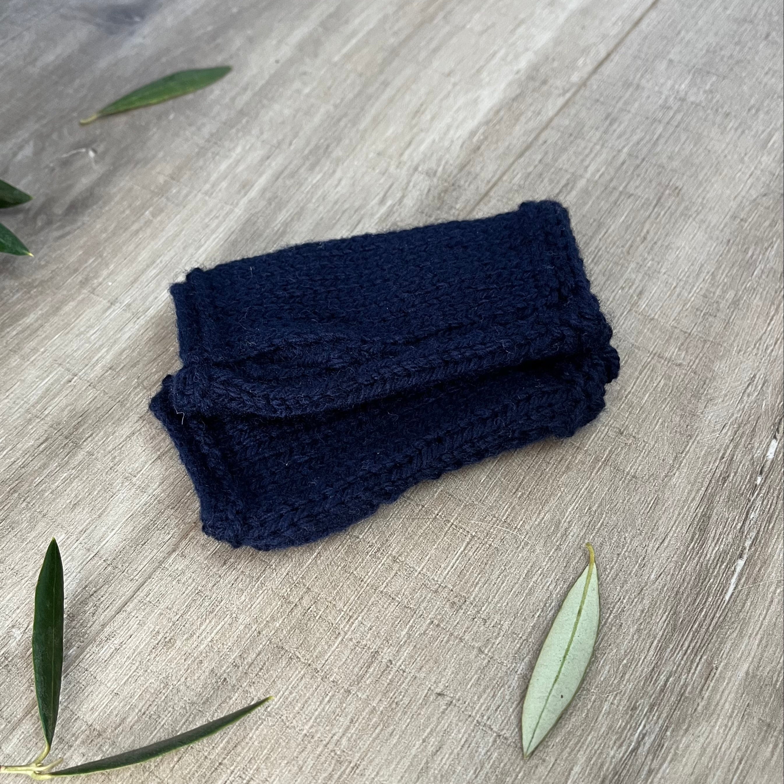 Navy knitted fingerless mittens on a wooden surface with olive leaves.