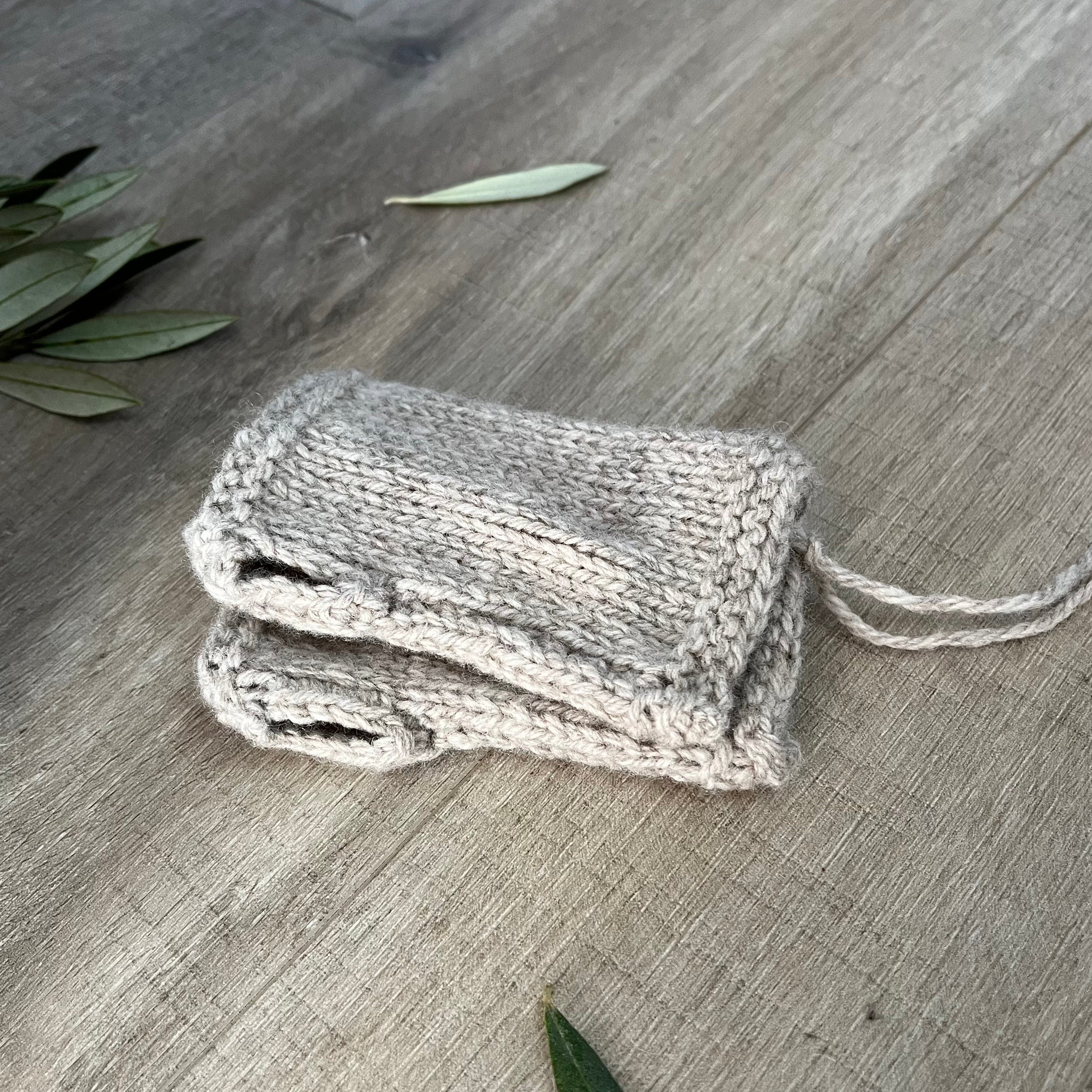 Oatmeal knitted fingerless mittens on a wooden surface with olive leaves.