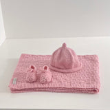 Knitted pink baby travel rug beanie and bootie set on white shelf