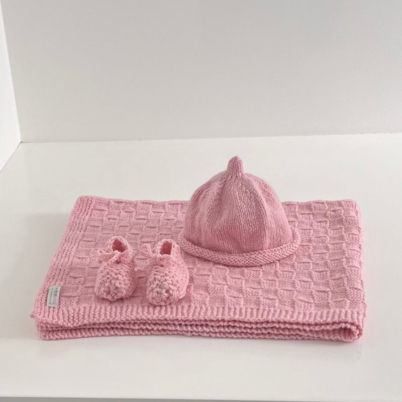 Knitted pink baby travel rug beanie and bootie set on white shelf