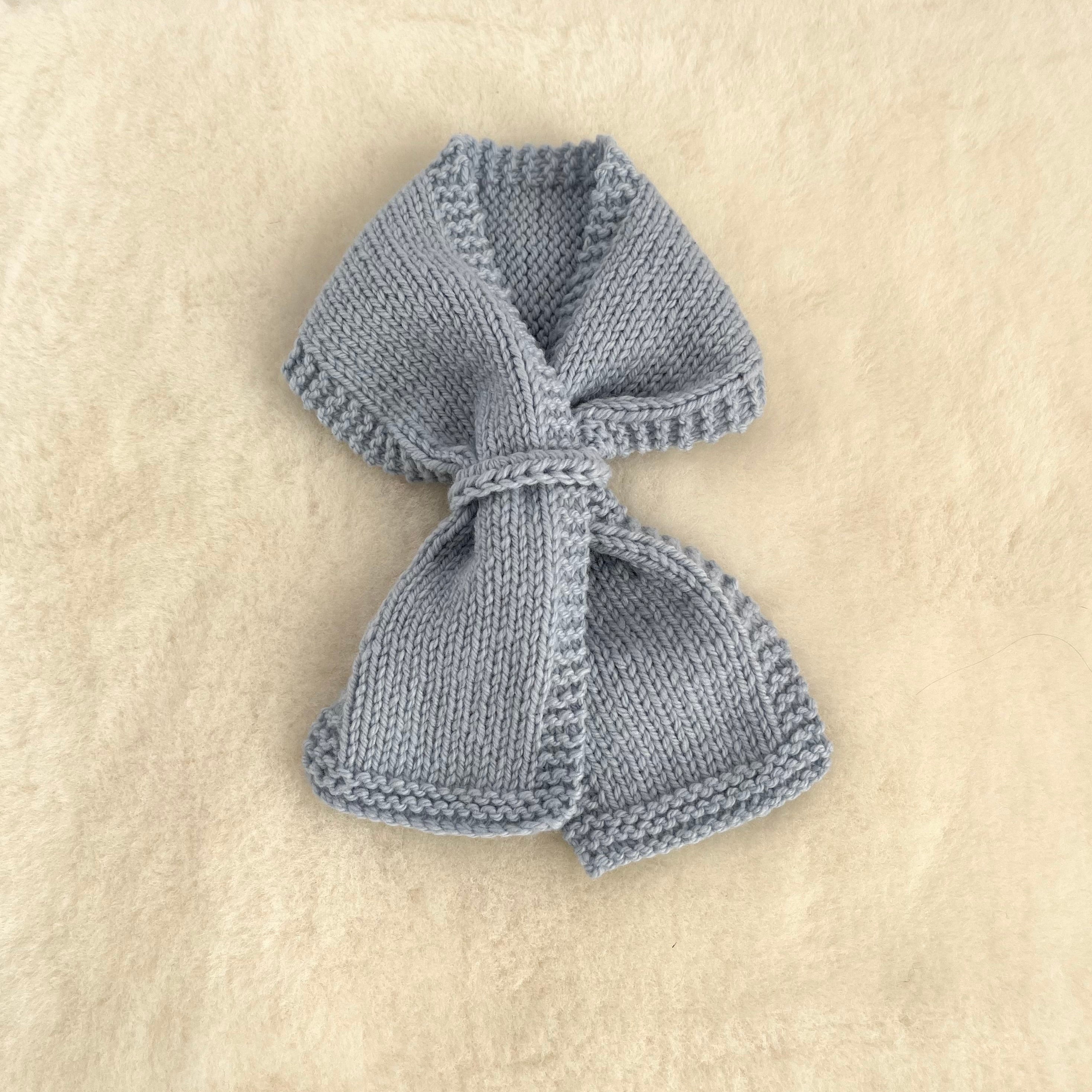 A small knitted loop scarf in blue, laid flat on a textured cream-colored fabric background.