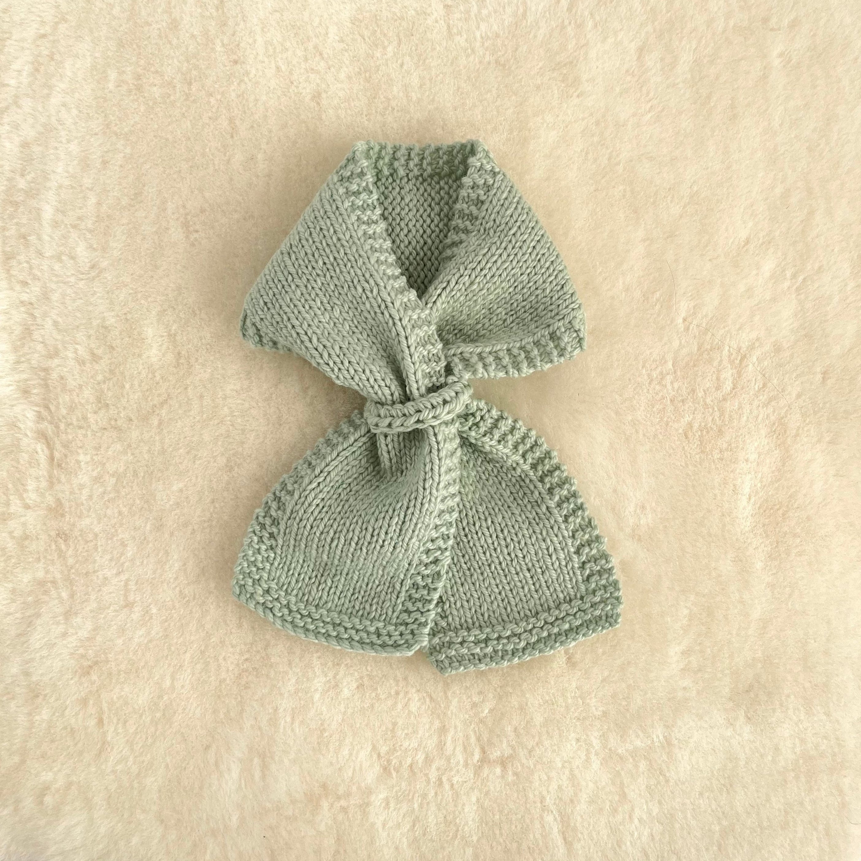 A small knitted loop scarf in mint, laid flat on a textured cream-colored fabric background.
