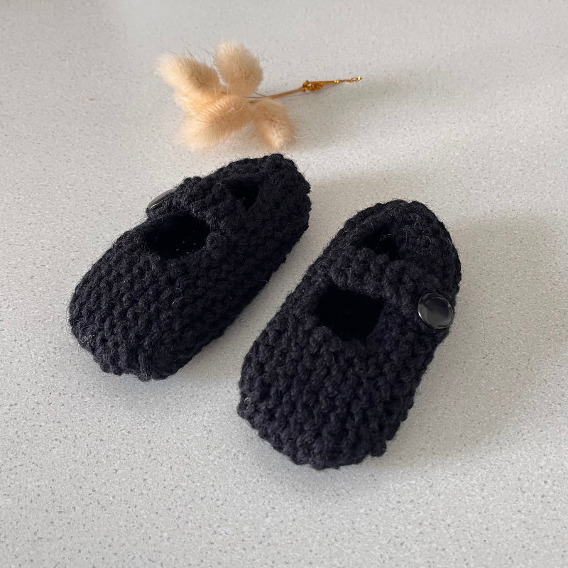 Pair of black knitted baby shoes on a light gray background