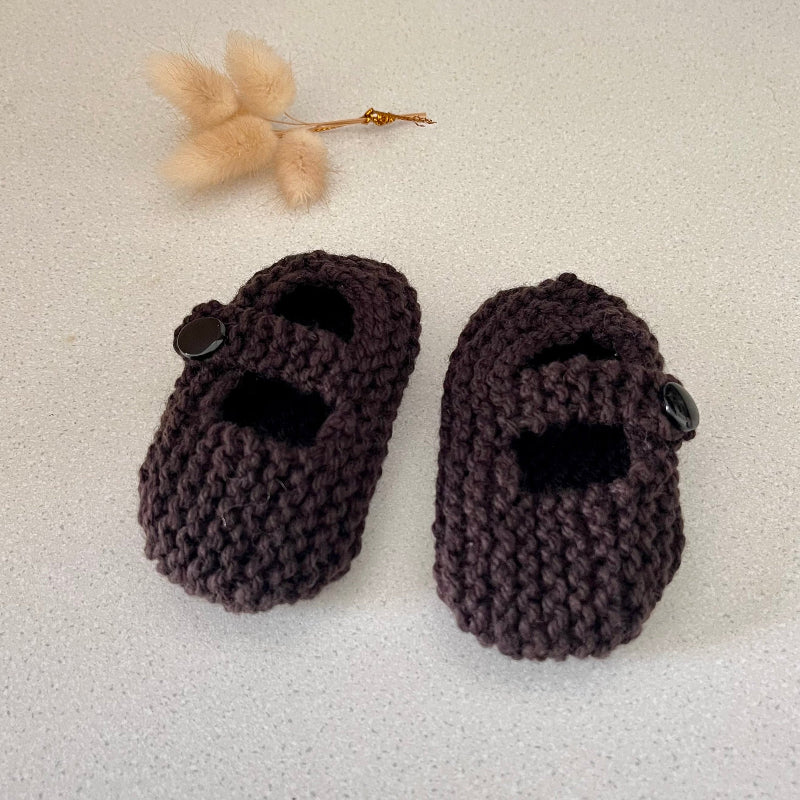 Pair of brown knitted baby shoes on a light background with a small decorative flower.