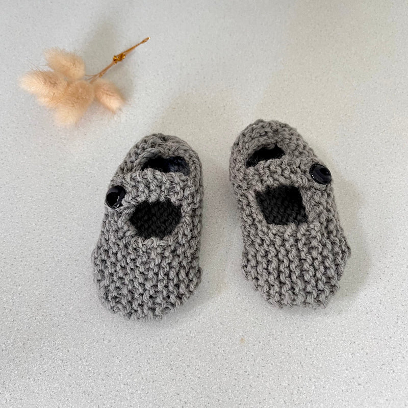 Pair of mushroom knitted baby booties on a light gray background
