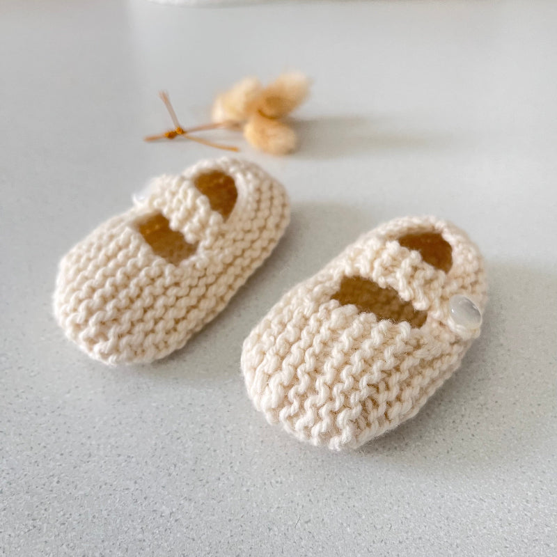 Pair of natural knitted baby shoes on a light grey surface