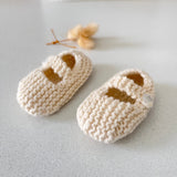 Pair of natural knitted baby shoes on a light grey surface