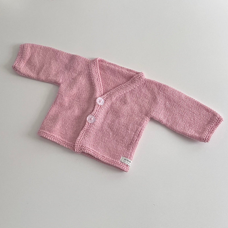 Knitted pink baby cardigan with buttons on a light grey background