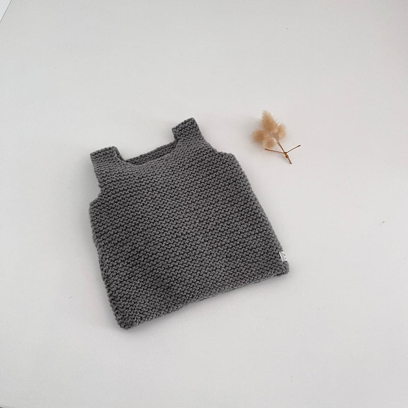 Knitted mushroom tank top on a white surface with a small dried plant.
