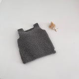 Knitted mushroom tank top on a white surface with a small dried plant.