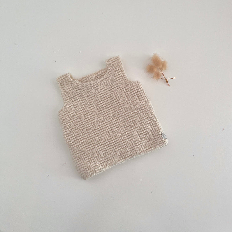 Knitted natural tank top on a white surface with a small dried 