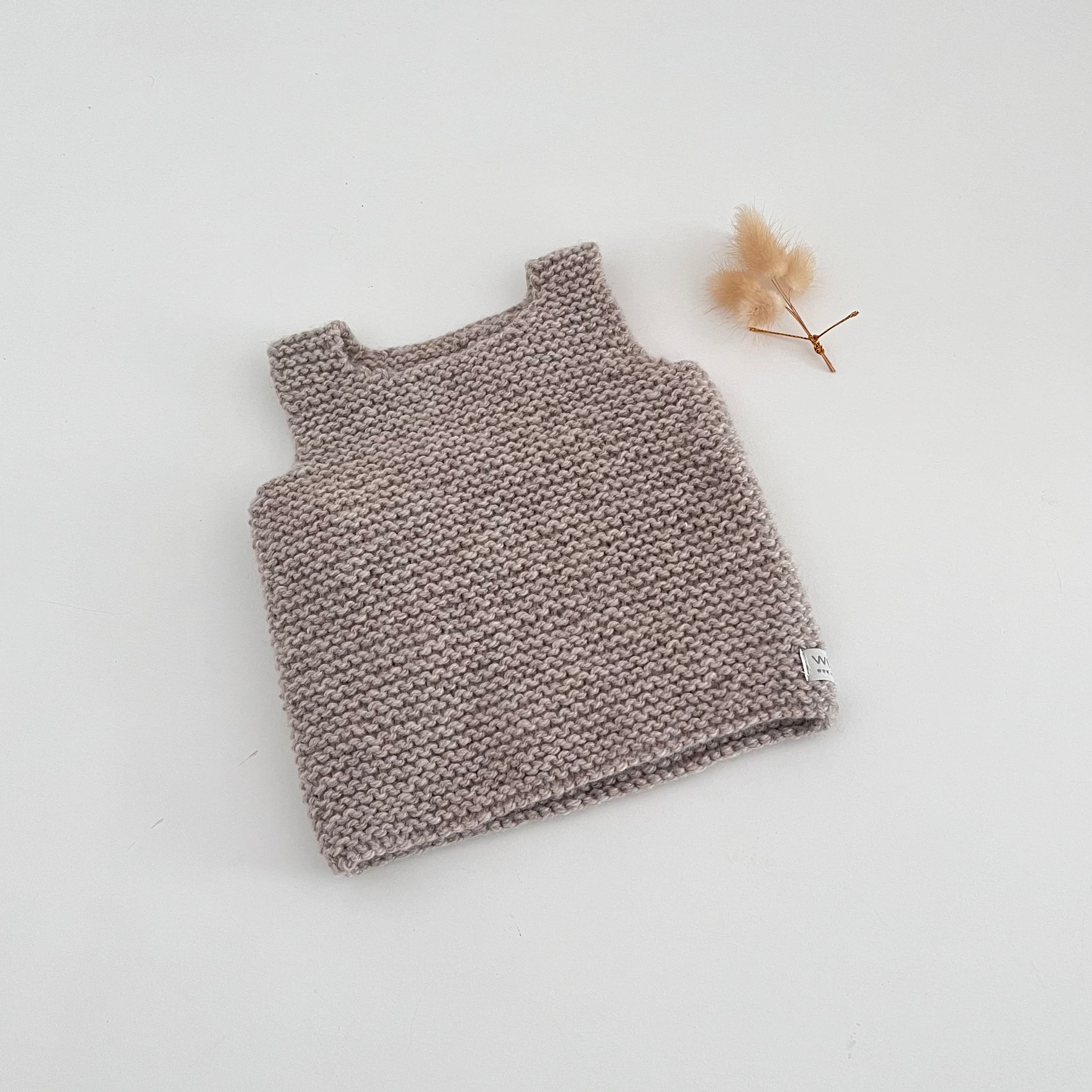 Knitted tank top on a light gray background with a small dried flower.