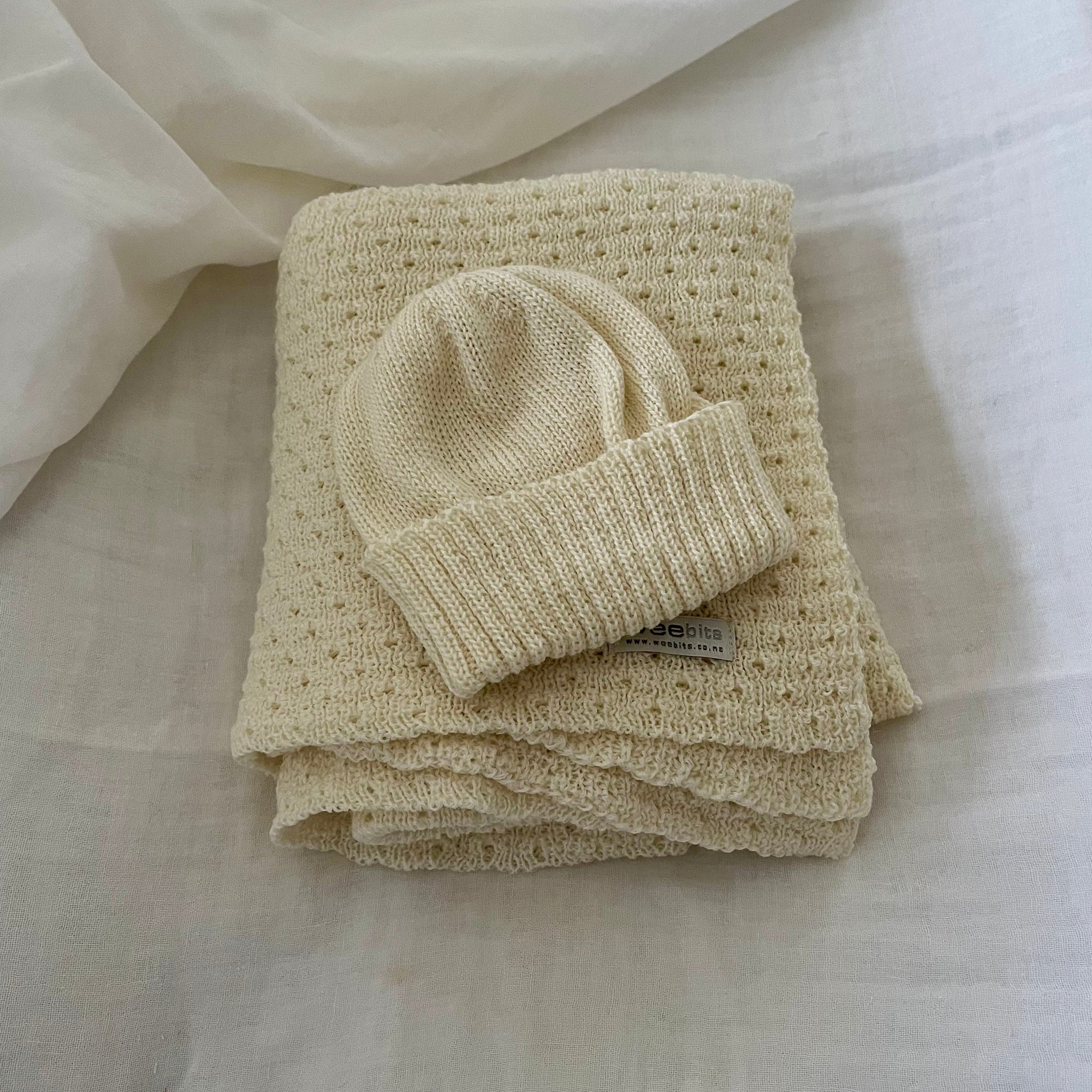 Folded  cream baby wrap with a matching beanie on a light fabric background