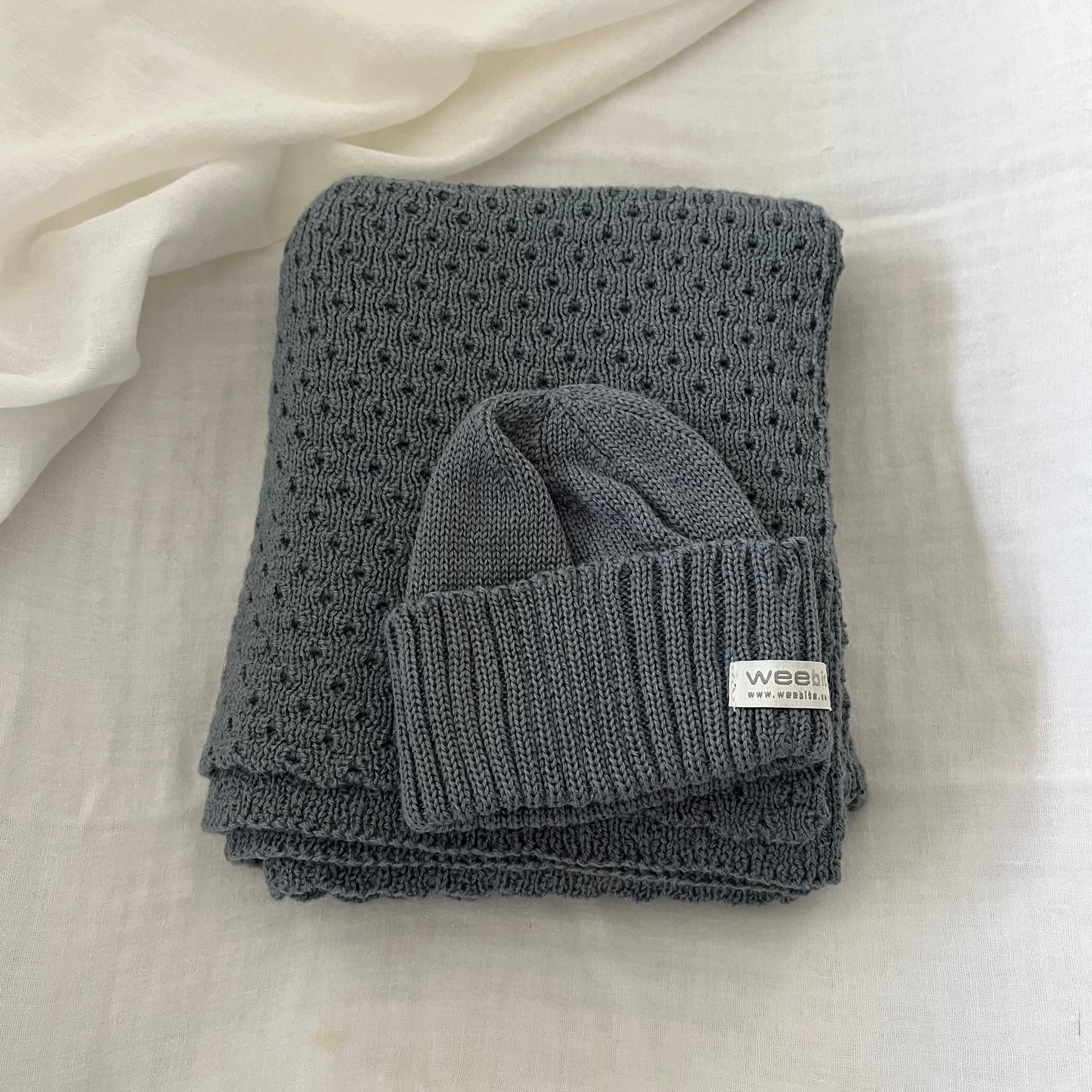 Folded  dusky blue baby wrap with a matching beanie on a light fabric background