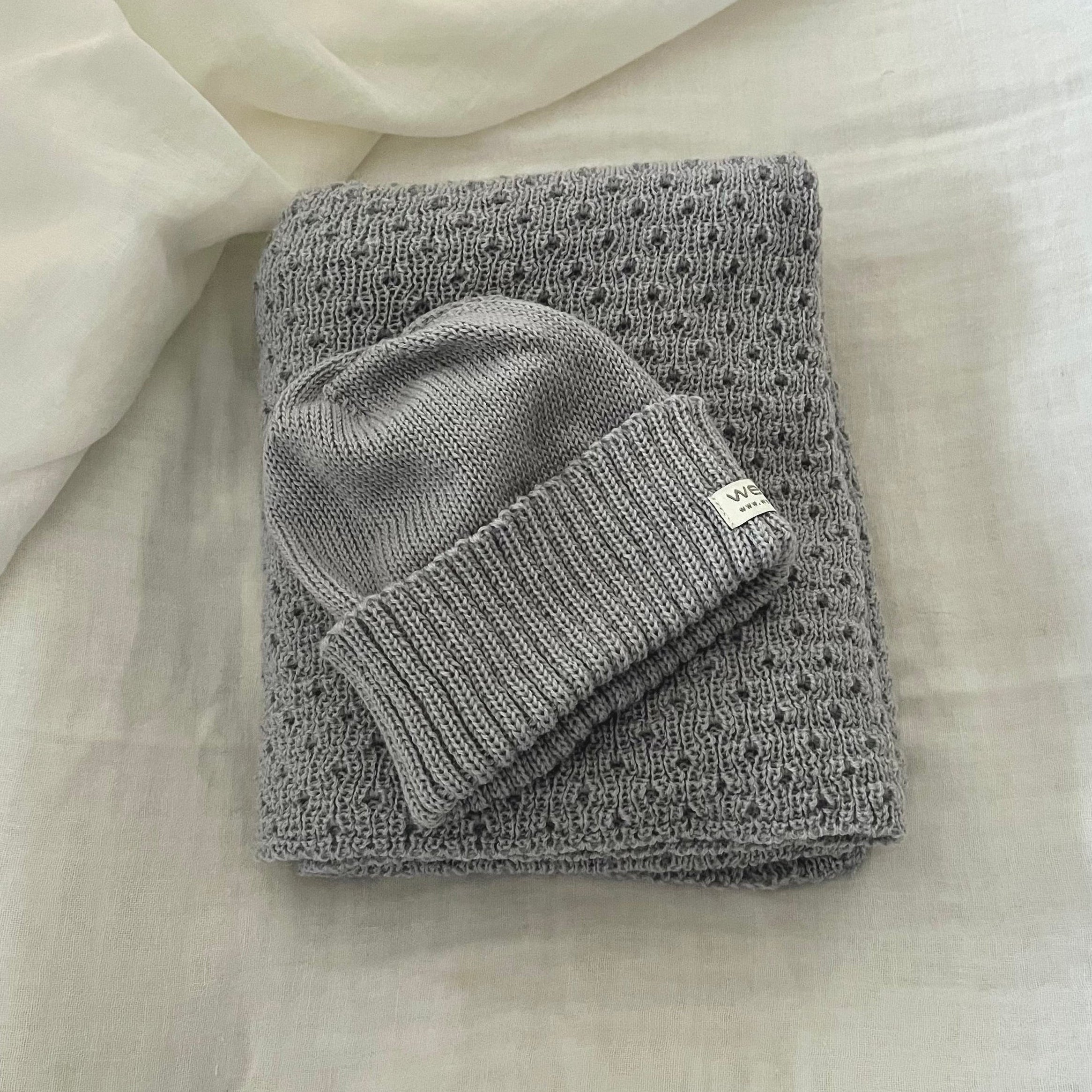 Folded  misty blue baby wrap with a matching beanie on a light fabric background