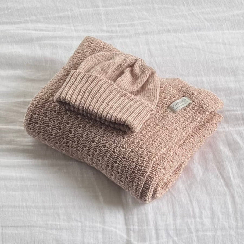 Folded sandstone baby wrap and matching beanie on a white textured surface