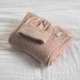 Folded sandstone baby wrap and matching beanie on a white textured surface