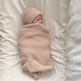 Newborn baby swaddled in a sandstone blanket and hat on a white background