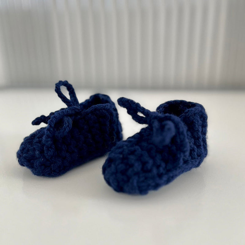 Pair of navy blue chunky knit booties on a white surface with a neutral background