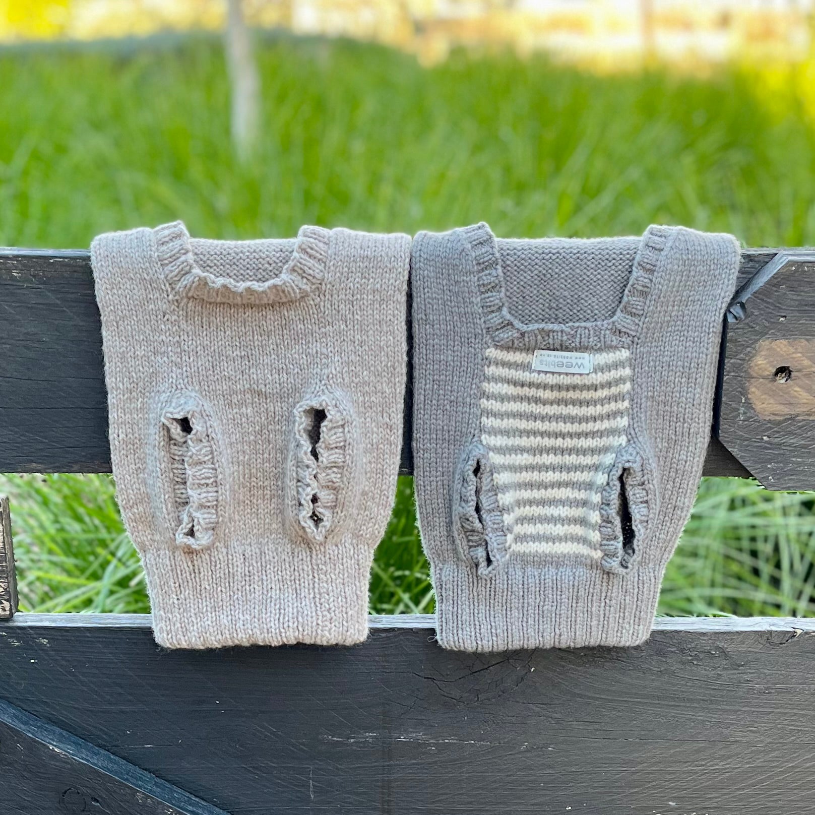 Two merino knitted dog jumpers draped over a fence wiht the bottom side showing
