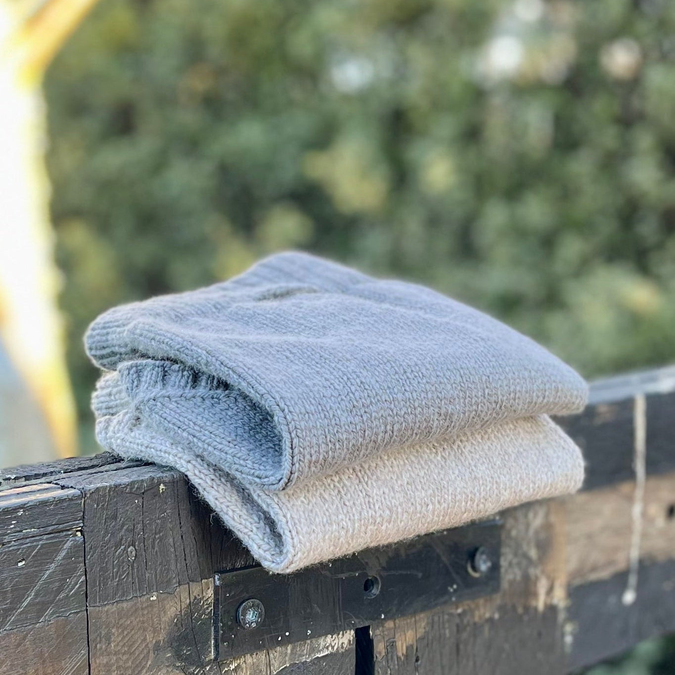 Two dog jumpres folded on a fence, in tan oatmeal and dark grey.