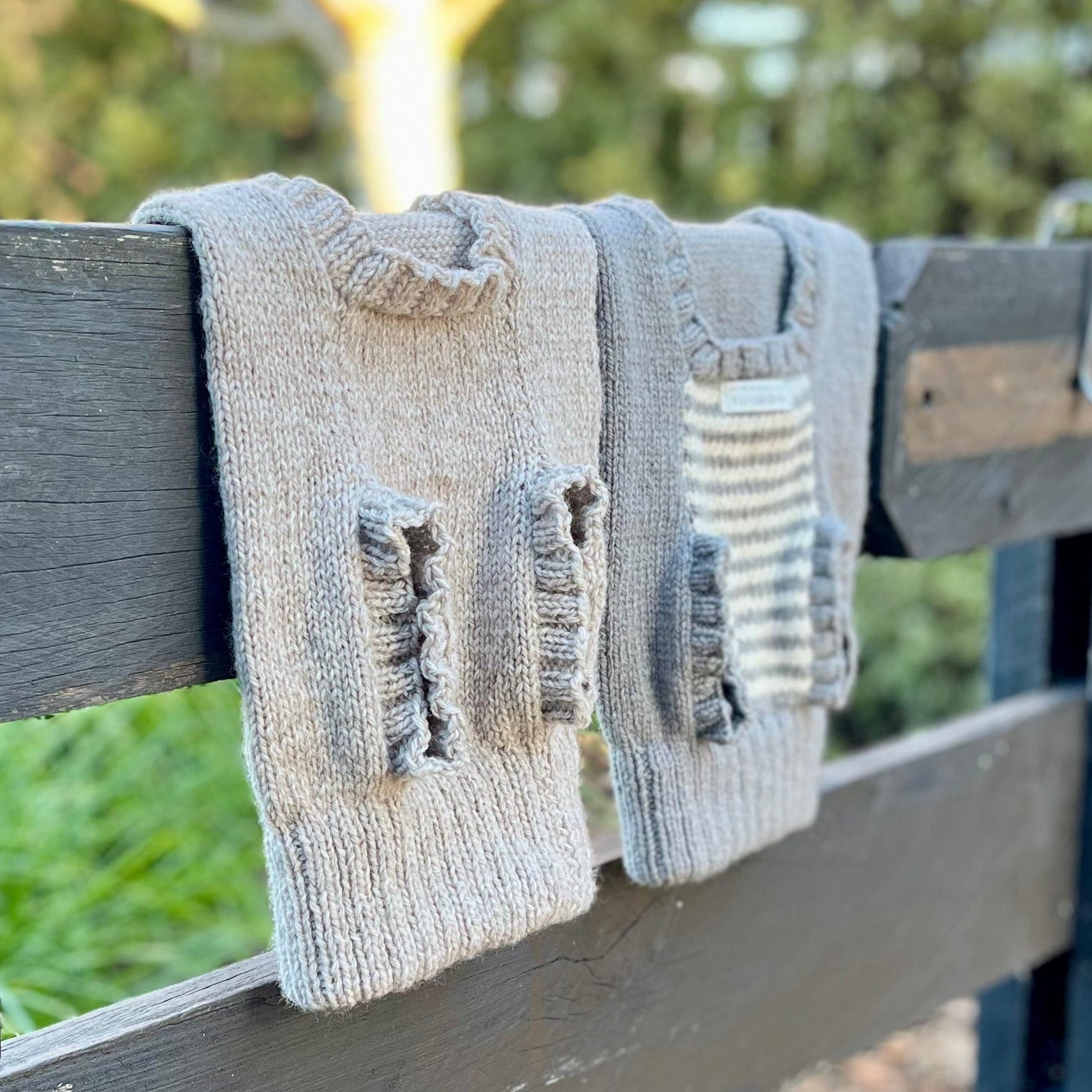 Two Weebits merino knit dog jumpers hanging from a fence. Oatmeal and mushroom natural stripe.