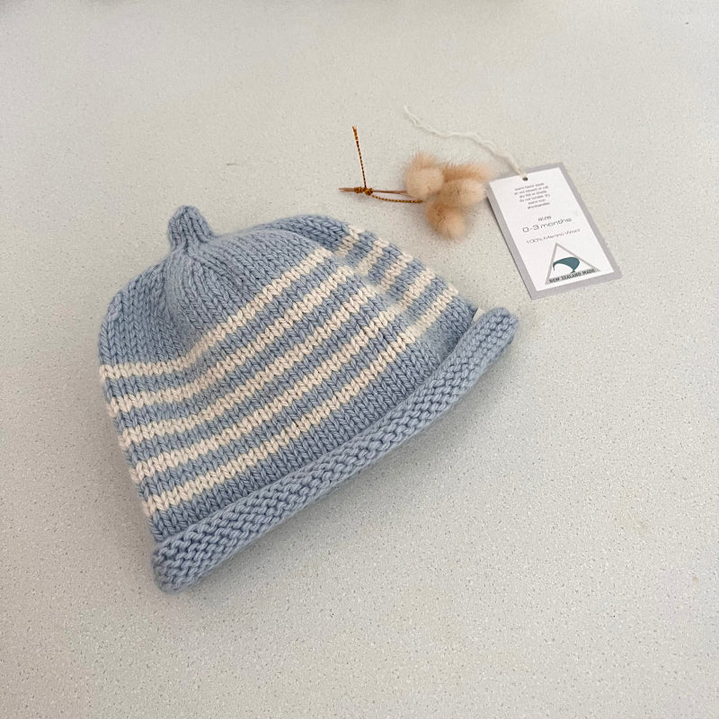 Blue and natural striped baby hat with a tag on a light grey background