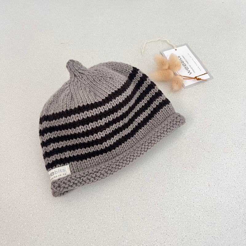 Mushroom and chocolate striped knit baby hat with a tag on a light grey background