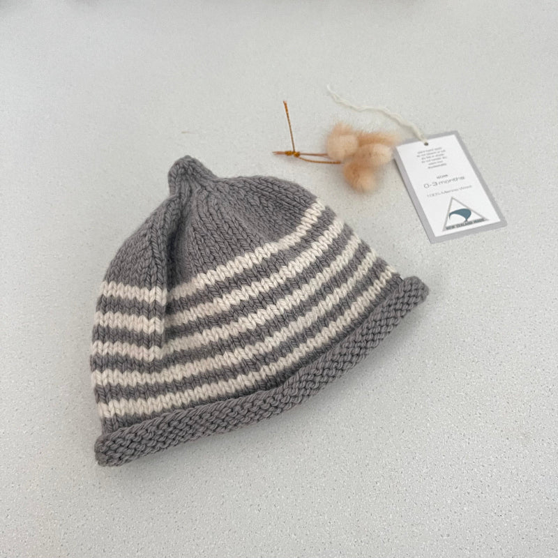 Mushroom and natural striped knit baby hat with a tag on a light grey background