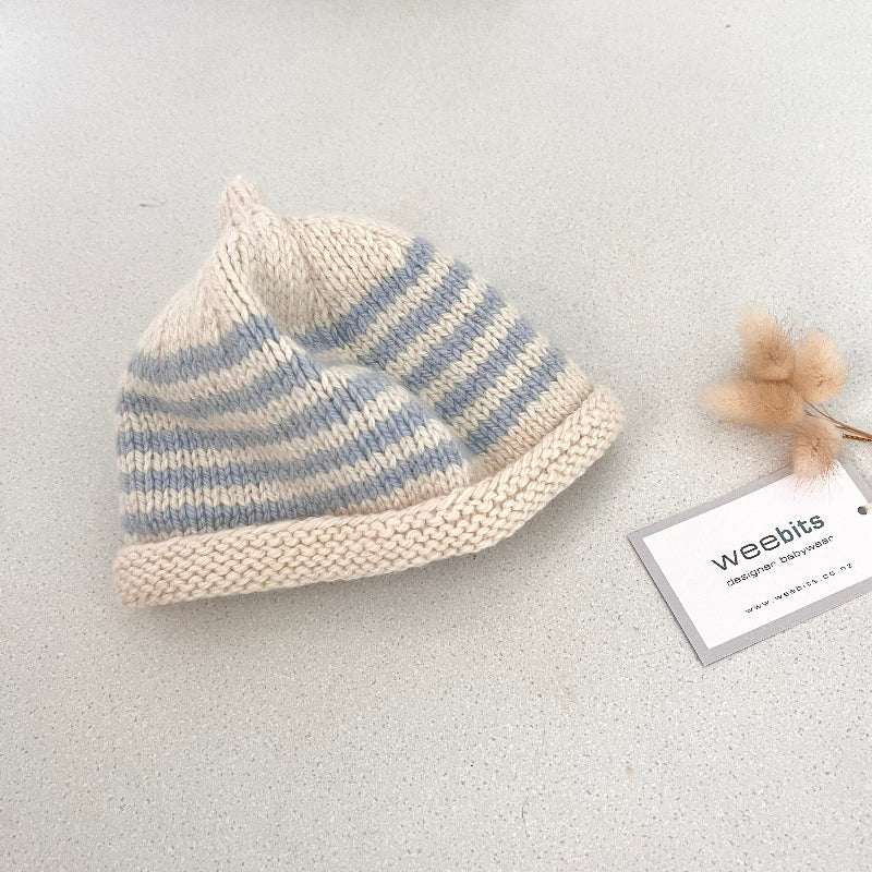 Natural and blue striped knit baby hat with a tag on a light grey background