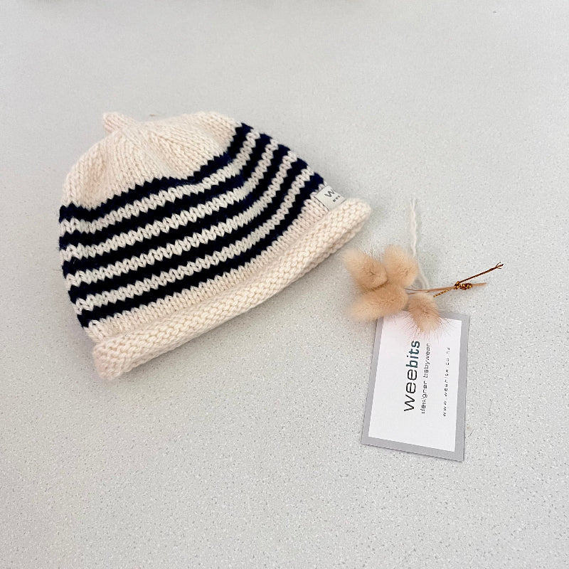 natural and chocolate striped knit baby hat with a tag on a light grey background