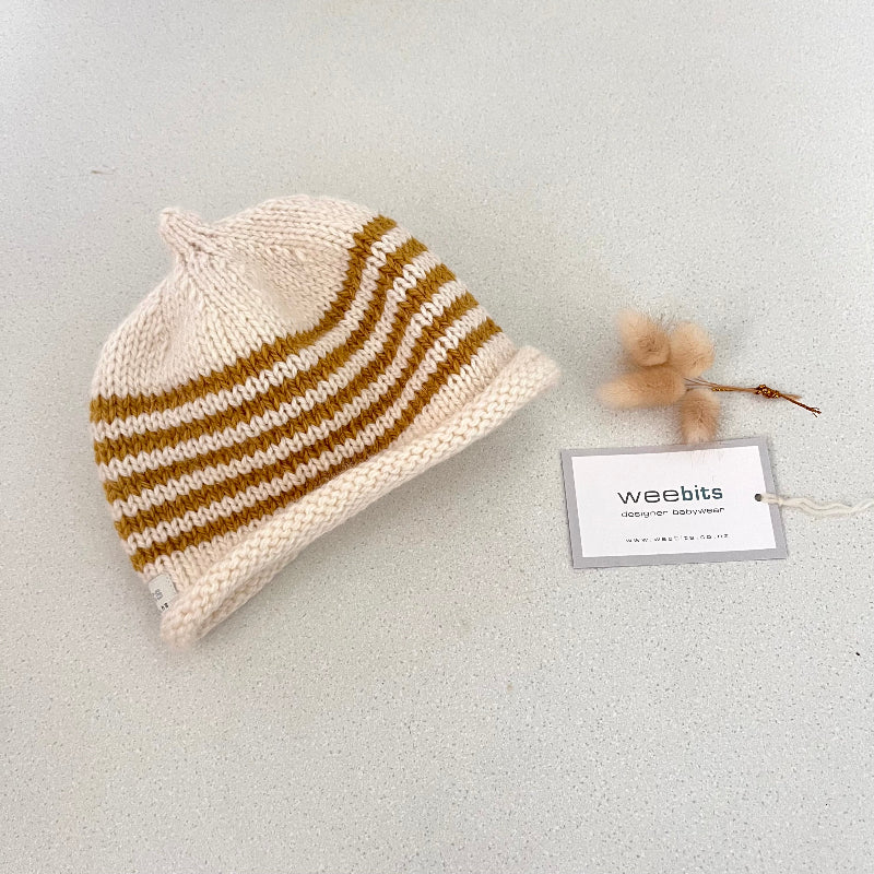 Natural and mustard striped knit baby hat with a tag on a light grey background