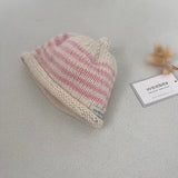 Natural and pink striped knit baby hat with a tag on a light grey background