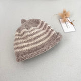 Oatmeal and natural striped knit baby hat with a tag on a light grey background