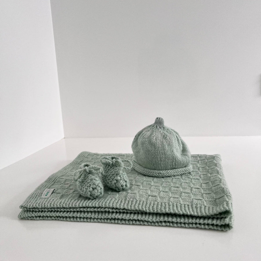 Mint baby hat and booties set on a folded green blanket against a white background