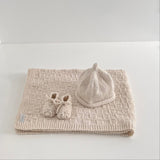 Knitted natural baby travel rug beanie and booties set on white shelf